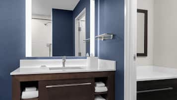 Een moderne badkamer met een witte wasbak, een grote spiegel en een donker houten opbergmeubel met handdoeken.