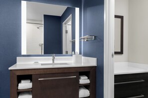 Un baño moderno con un lavamanos blanco, un espejo grande y un mueble de tocador de madera oscura con toallas.