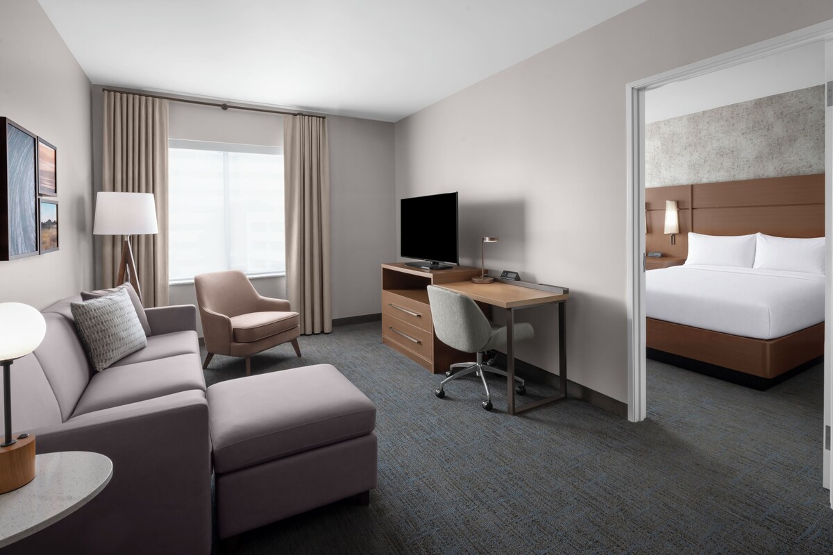 A hotel room with a bed, a desk, a chair, a sofa, a television, and a window with curtains.