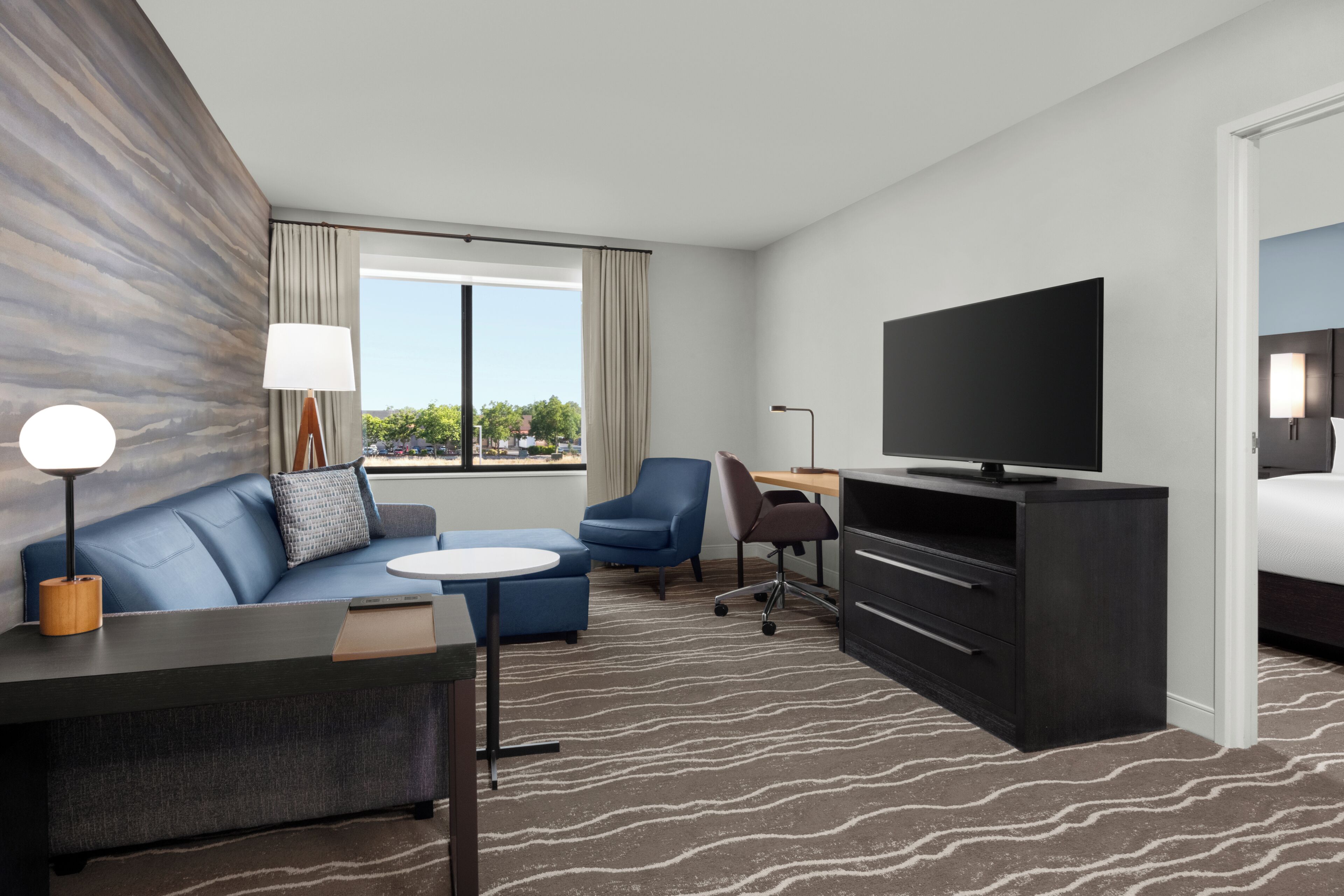 A modern hotel room with a sofa, a small table, a TV, a desk, and a bed.