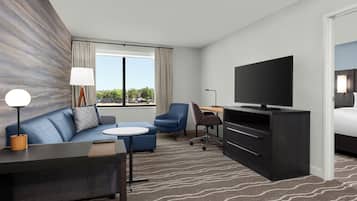 A modern hotel room with a sofa, a small table, a TV, a desk, and a bed.