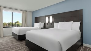 A hotel room with two beds, a large window, and a view of the outdoors.
