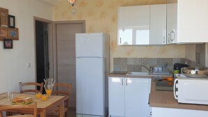 A compact kitchen with a refrigerator, a sink, and a dining area with chairs and a table. - Charming apartment with a panoramic view of the sea. 5 minutes from the beaches (Valle-di-Campoloro)