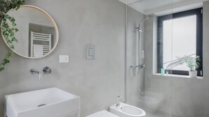 Un bagno moderno con un lavandino ampio, due servizi igienici, una doccia e una finestra con una pianta.