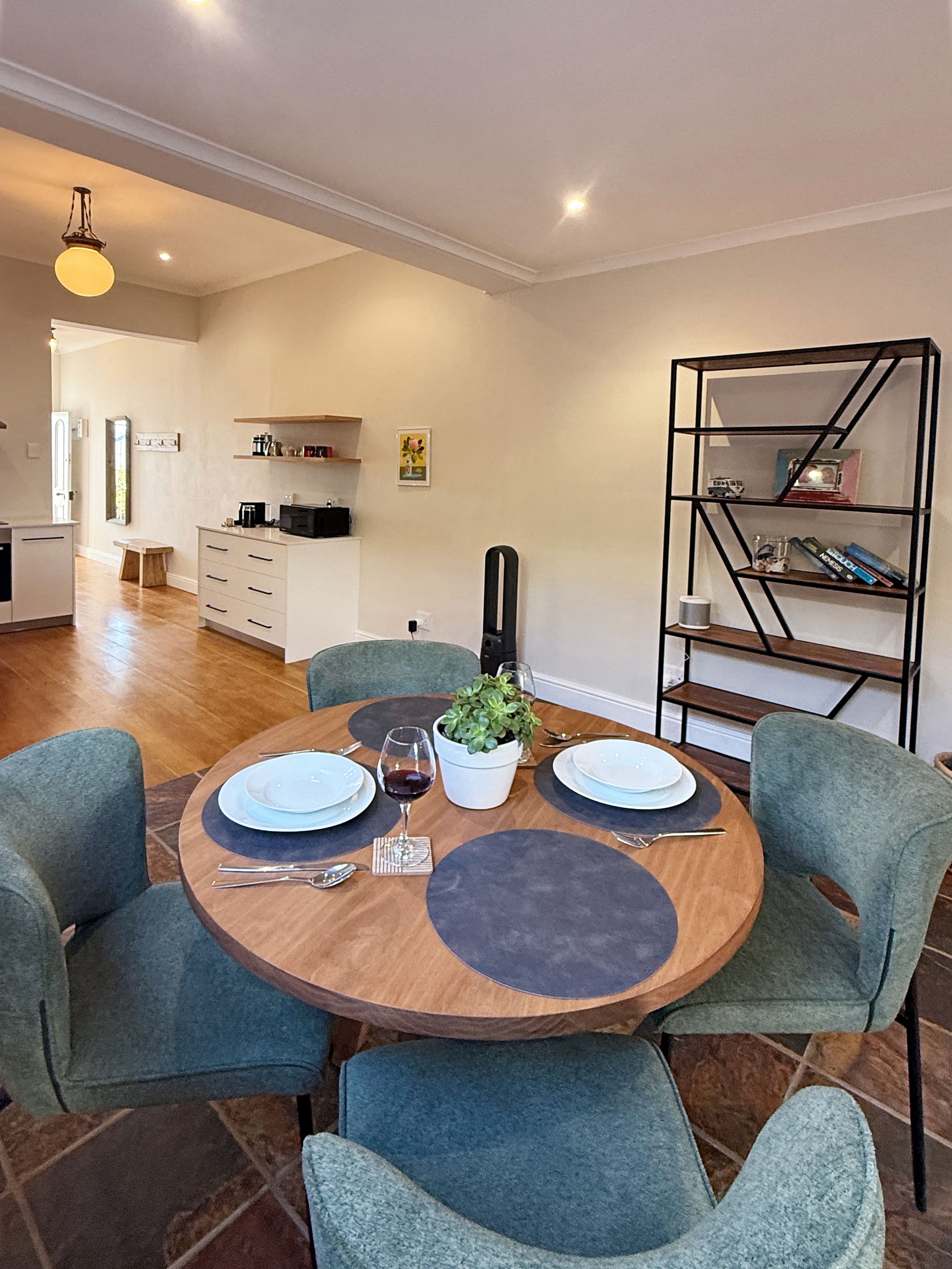 A dining area with a round table set for two, surrounded by teal chairs.
