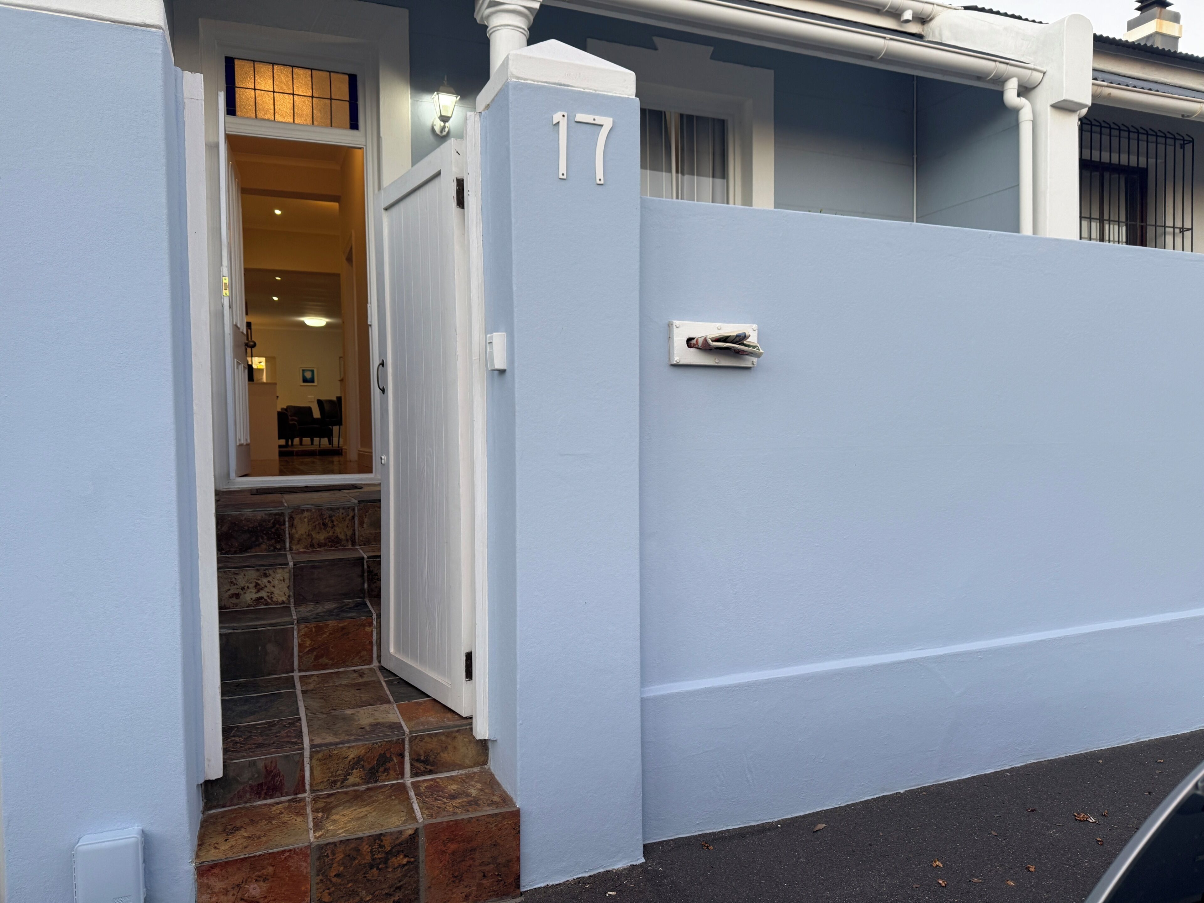 A residential property with a white exterior, a number '17' sign, a tiled entrance, and a visible interior with a dining area.