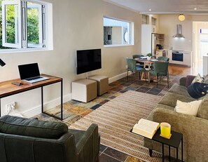 A modern living room with a sofa, a coffee table, a TV, and a laptop on a desk.
