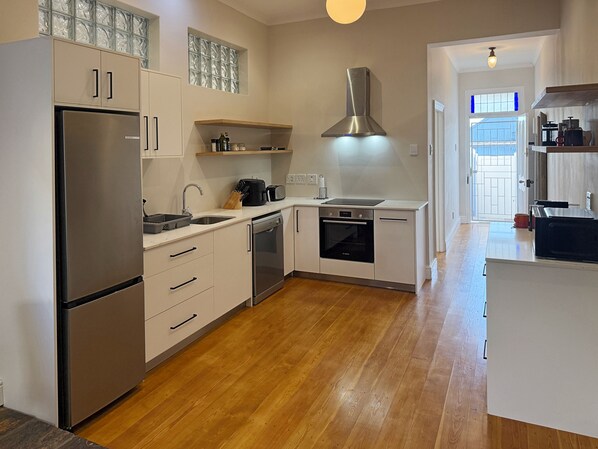 A modern kitchen with a stainless steel refrigerator, dishwasher, oven, and a range hood. There is a window with a decorative glass panel above the sink, and a wooden countertop with various kitchen items.