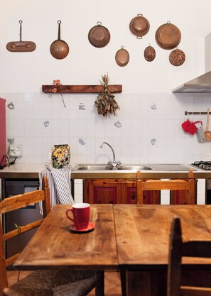 Uma cozinha com mesa de madeira, cadeiras, pia e diversos utensílios de cozinha pendurados na parede.