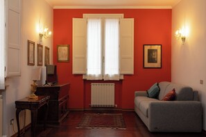Quarto com parede vermelha, sofá cinza, armário de madeira e radiador.