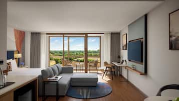 Una habitación de hotel moderna con un ventanal grande, un sofá, un escritorio y un televisor.