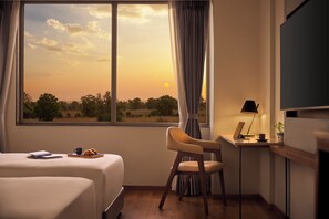 Una habitación de hotel con un ventanal grande, una cama, un escritorio con una computadora portátil, una silla y un televisor.