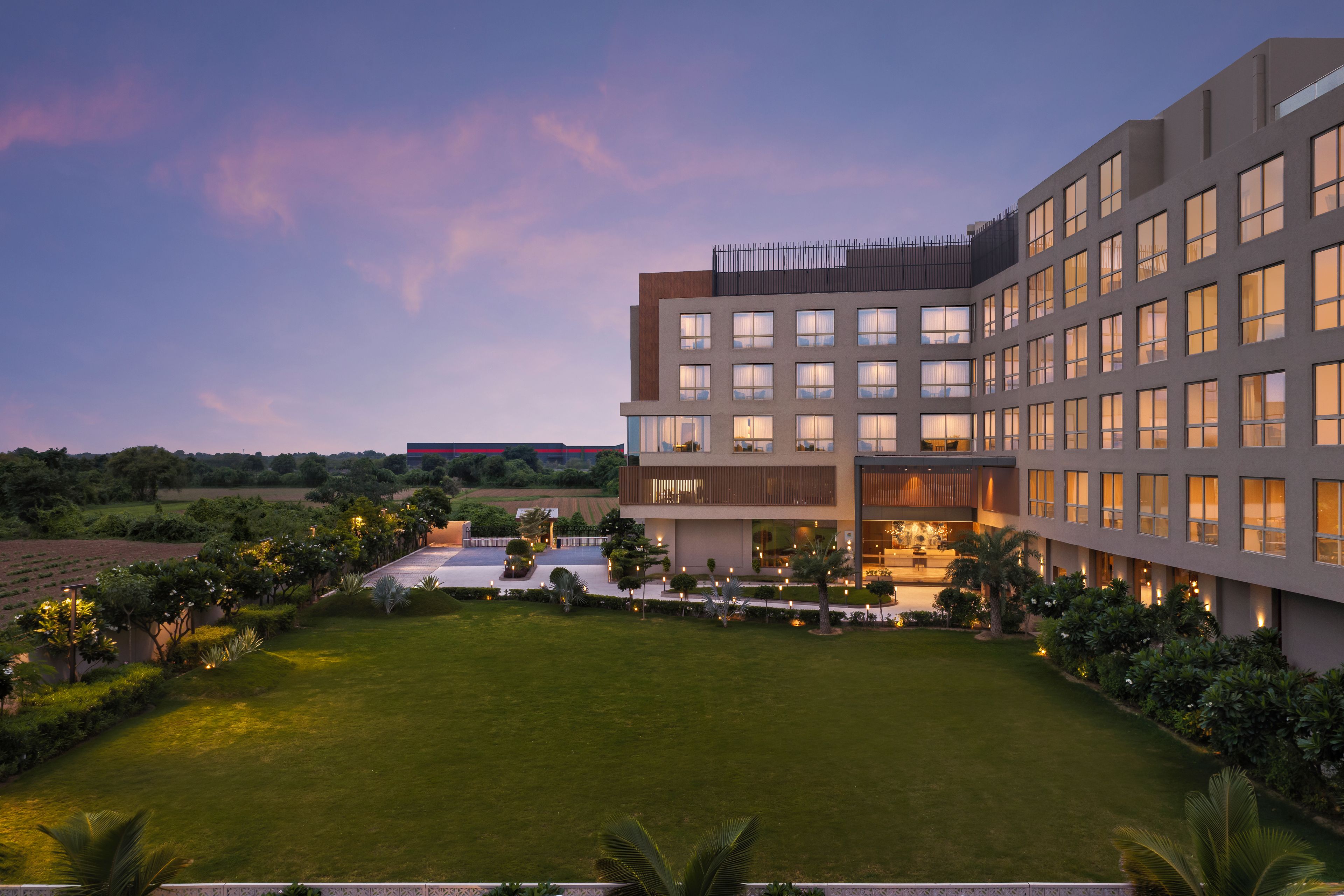 A modern hotel with multiple floors, a well-maintained lawn, and a landscaped garden.