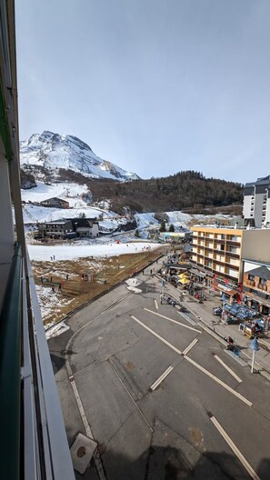 A view of a parking lot with a mountain in the background, a building with multiple floors, and a restaurant with outdoor seating. - Studio apartment at the base of the ski lifts (Eaux-Bonnes)