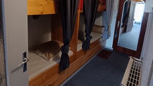 Un lit superposé avec une structure en bois, une petite table de chevet, un miroir et une porte avec une poignée.