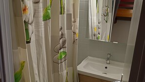 Une salle de bain avec un rideau de douche orné d’un motif naturel, un lavabo avec un miroir au-dessus et un meuble-lavabo en bois.