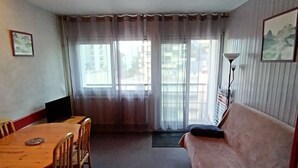Une pièce comprenant une table à manger en bois, des chaises, un canapé, un lampadaire et une fenêtre avec des rideaux.