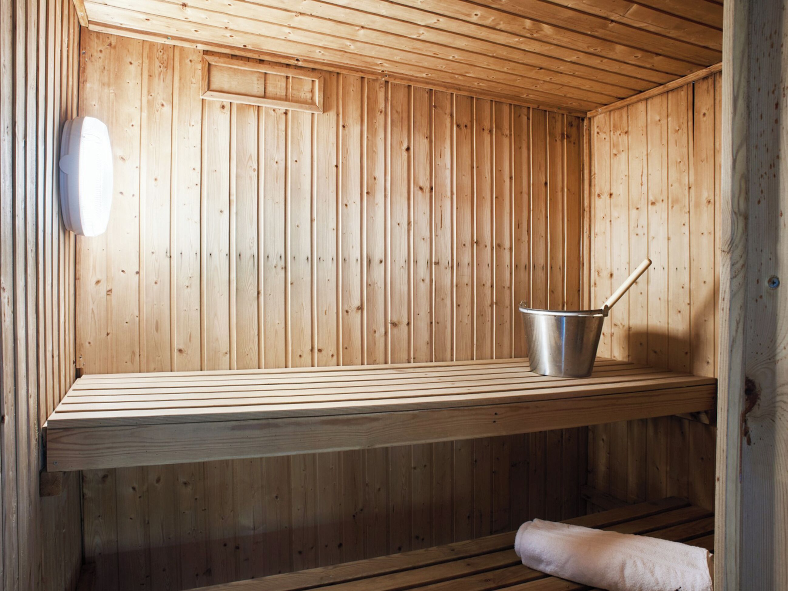 A sauna with wooden walls, a bench, a bucket, and a towel.