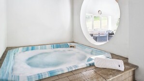 Een bubbelbad met uitzicht op een terras buiten, zichtbaar door een rond raam.