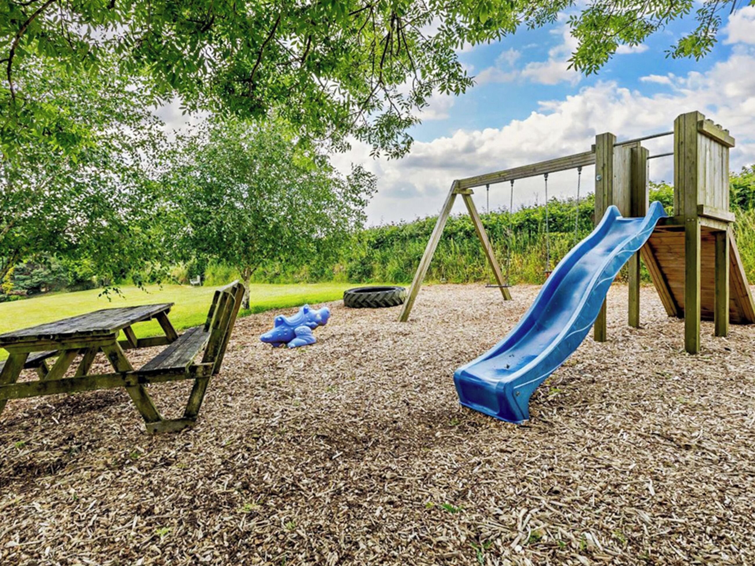 Une aire de jeux avec un toboggan, des balançoires et des tables de pique-nique.