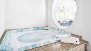 Een bubbelbad in een hoek, met uitzicht op een kamer via een ronde spiegel.