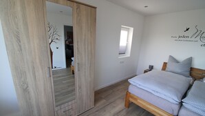 Une chambre avec une armoire en bois, un lit avec des oreillers, une fenêtre et un motif décoratif sur le mur.