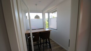 Une pièce avec un plancher en bois, une table à manger avec des chaises et une fenêtre avec des stores.