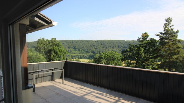 Un balcon donnant sur une colline boisée, avec une rambarde en métal et un sol en béton.