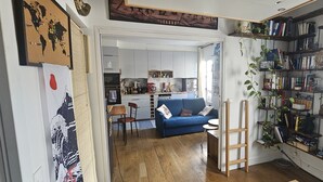 Un espacio habitable compacto con kitchenette, un sofá azul, una escalera de madera y una estantería llena de libros y plantas.