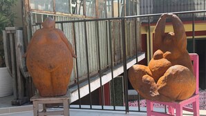 Dos esculturas en un balcón con barandilla de metal y una escalera al fondo.