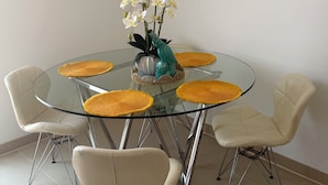 Una mesa redonda de vidrio con manteles individuales amarillos, rodeada de sillas blancas con patas de metal.