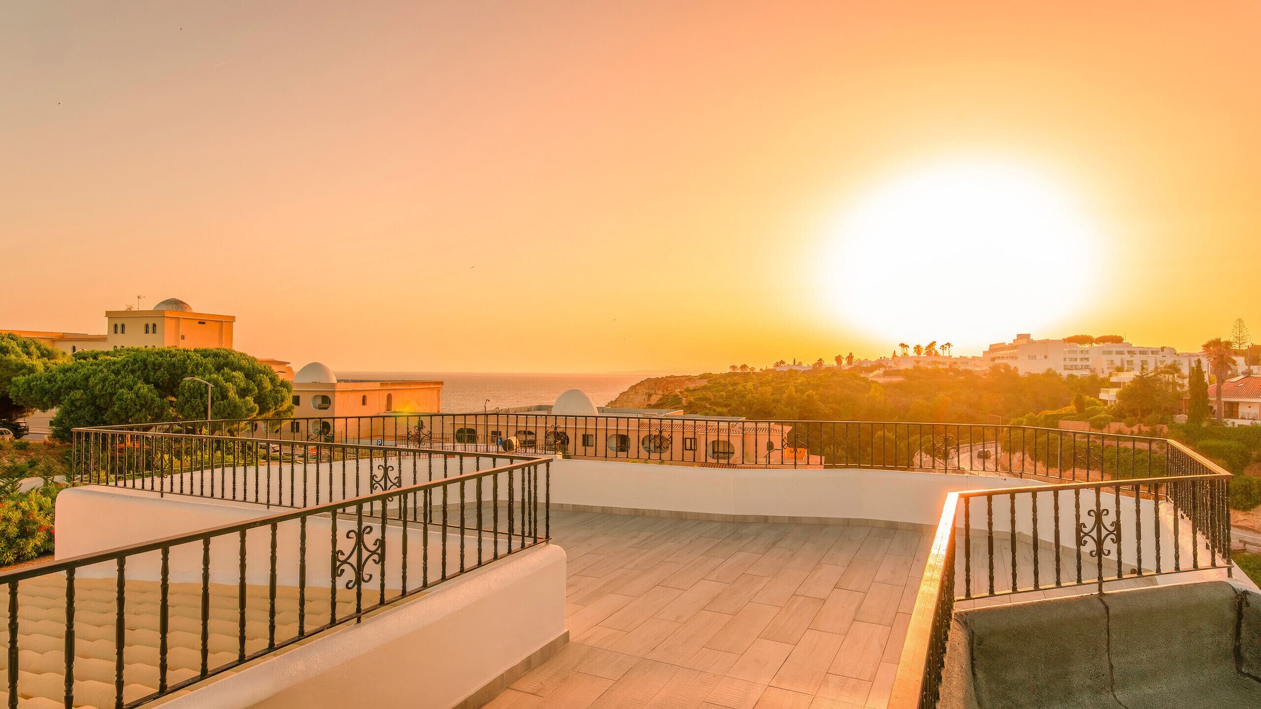 A rooftop terrace with a view of the sea and buildings during sunset.