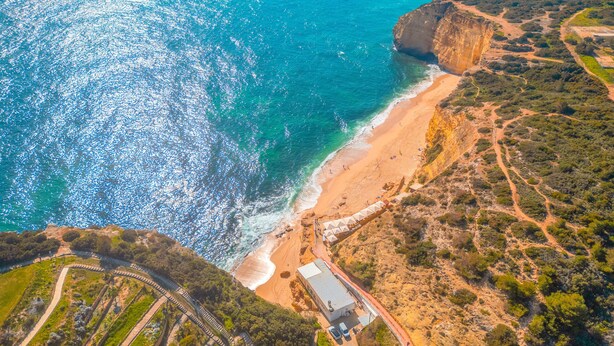 Eine Luftaufnahme einer Küstenlandschaft mit Strand, Klippen und einem Gebäude mit Flachdach.