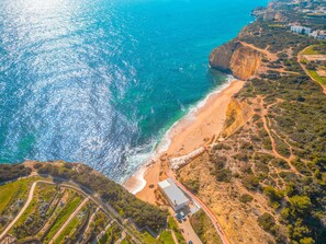 Eine Luftaufnahme einer Küstenlandschaft mit Strand, Klippen und einem Gebäude mit Flachdach.