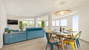 Ein modernes Wohnzimmer mit einem blauen Sofa, einem Esstisch mit Stühlen und einem an der Wand befestigten Fernseher.
