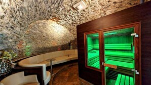 A spa area with a stone wall, a wooden bench, and a glass-enclosed sauna. - Hotel Öhlknechthof (Horn)