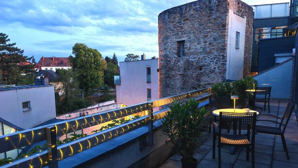 A rooftop terrace with a stone wall, a railing with string lights, and outdoor seating. - Hotel Öhlknechthof (Horn)