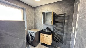 A modern bathroom with a washing machine, a wooden cabinet, a sink, and a towel rack.