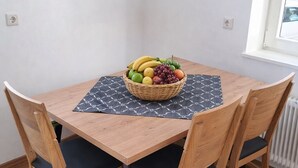 A wooden dining table with a woven fruit basket, dark patterned placemat, and matching chairs.