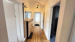 A hallway with wooden flooring, a kitchen area with a wooden countertop, a black tiled shower area, and a ceiling light fixture. - Litzldorf (Sankt Martin)