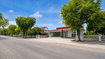 Eine Tankstelle mit rotem Vordach, weißem Zaun und Bäumen entlang der Straße.
