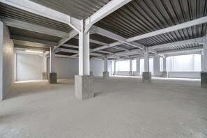 An empty industrial-style interior with concrete pillars, a high ceiling, and large windows.