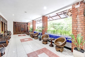 Vestíbulo de hotel con suelo de baldosas, sillas de madera, un mostrador de recepción y vistas a zonas verdes.
