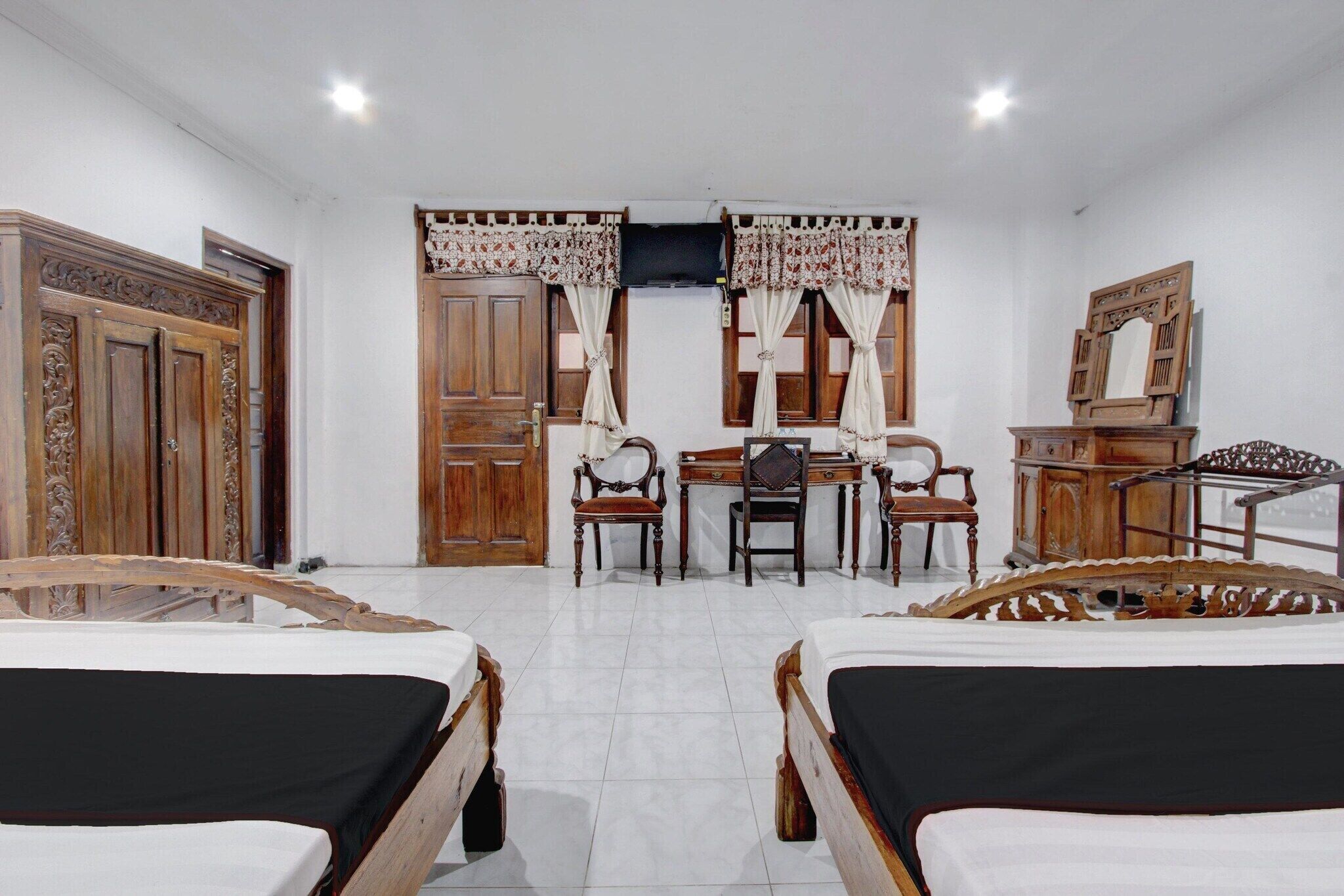 Una habitación con dos camas de madera, un escritorio con sillas, un espejo y un armario.