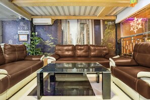 Um hall moderno com um sofá de couro marrom, uma mesa de centro de vidro e vista para a cidade por uma grande janela.