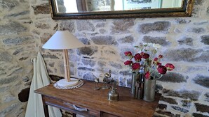 A wooden desk with a lamp, a vase with flowers, and a mirror on a stone wall. - Stone house in Brittany by the sea (Lannilis)