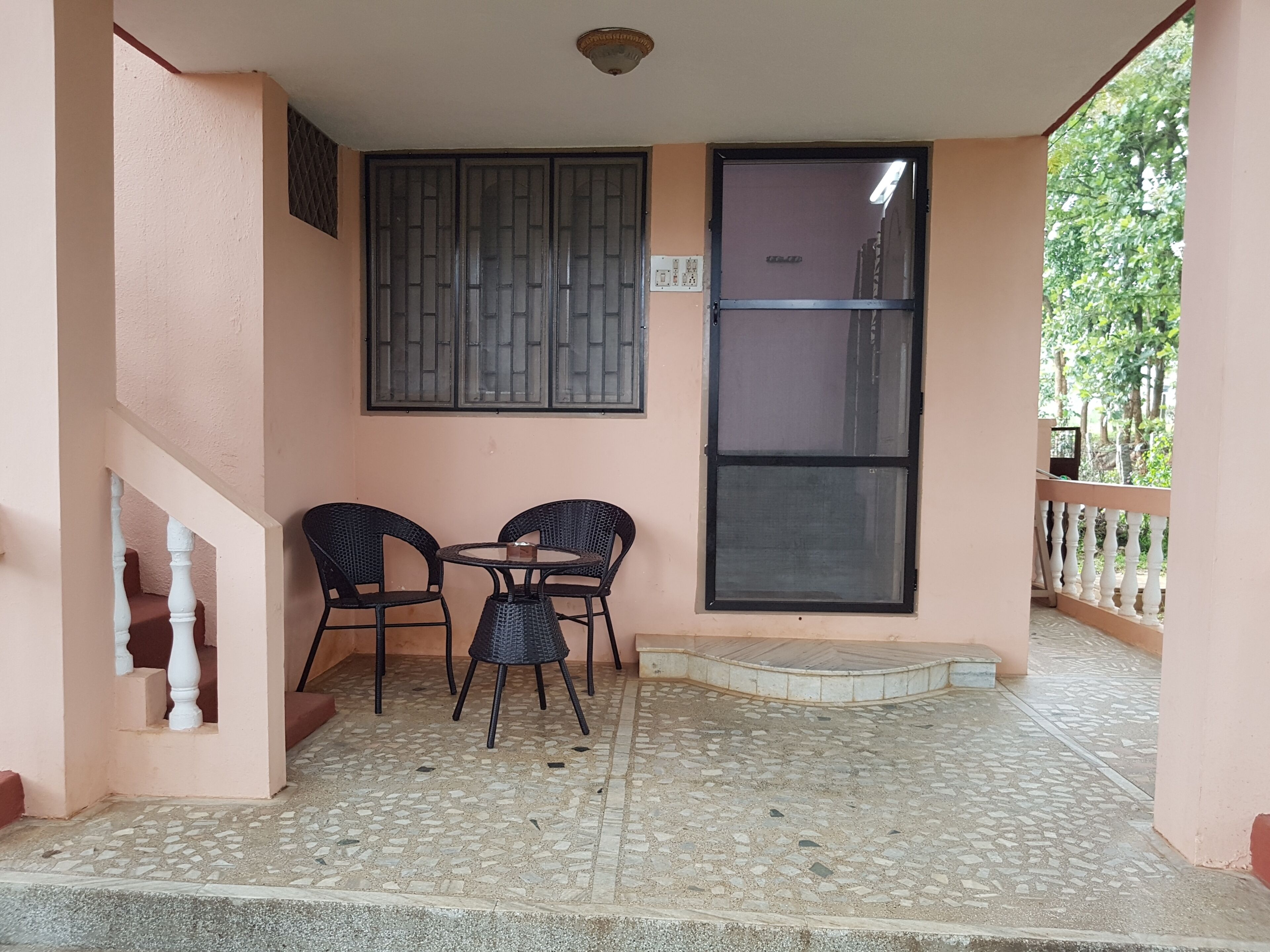 A covered outdoor area with a tiled floor, a table with chairs, a window, and a staircase.