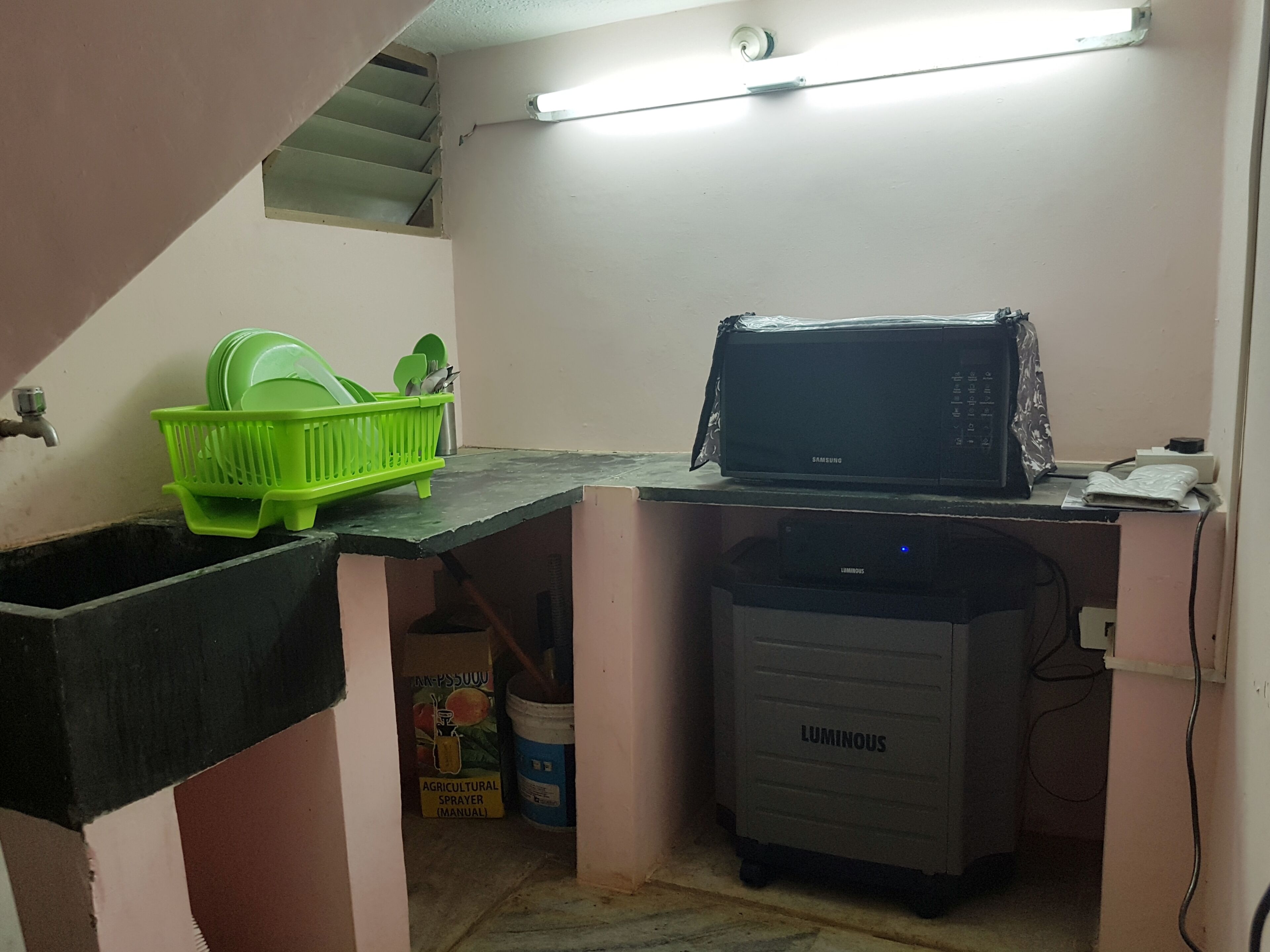 A compact kitchen with a microwave, a water dispenser, and a green dish rack.