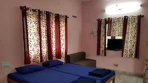 Une chambre avec deux lits, un canapé, une télévision et des rideaux à motifs.