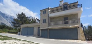 A two-story building with a balcony, two garages, and a mountainous backdrop. - 2-Story Stone House in Bonaca - Ocean View & Privacy (Baška Voda)